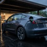 Tesla Model 3 charging at a residential carport on a rainy evening.